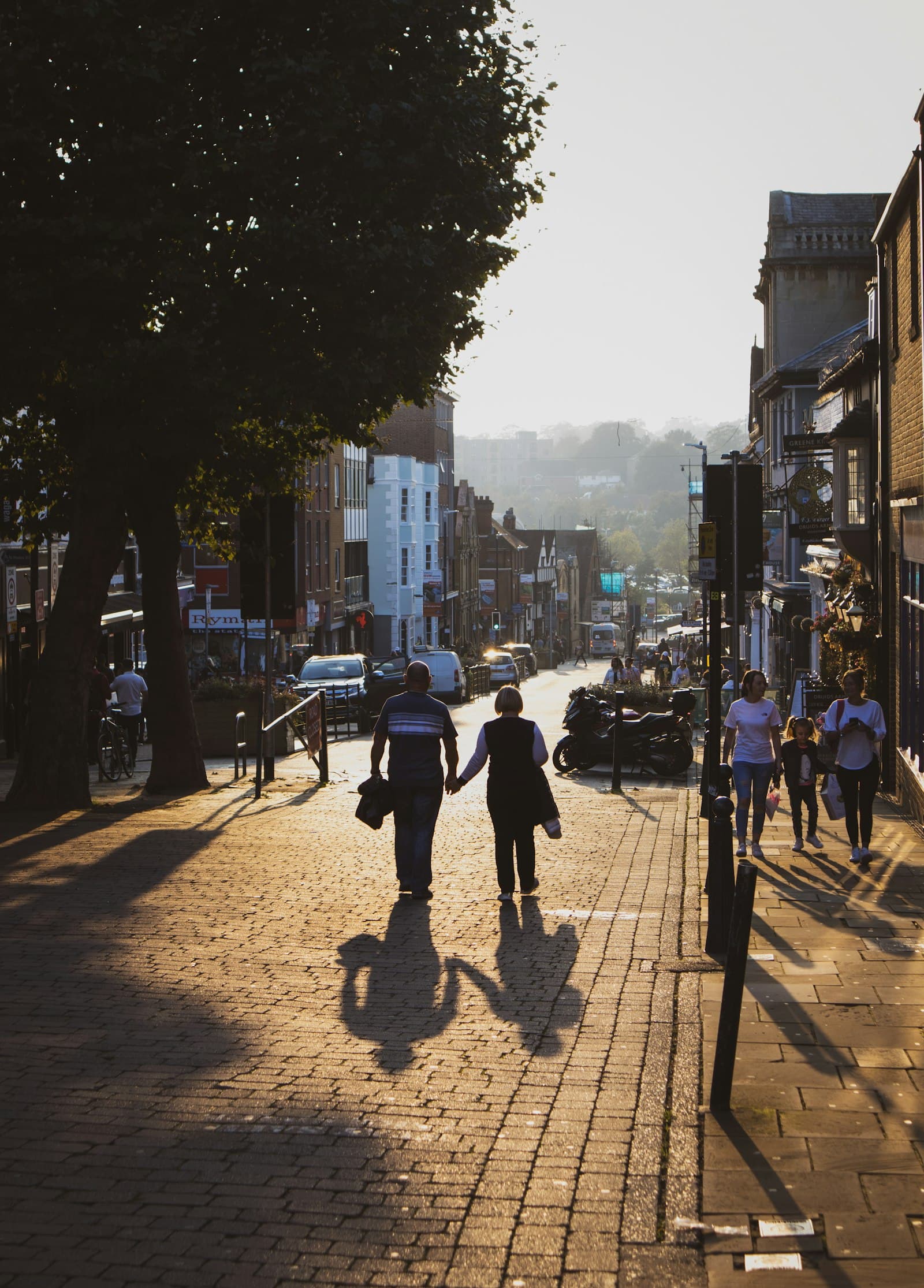 A couple walking down a sunlit street holding hands — partnership and shared work